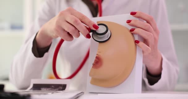 Женщина-врач применяет стетоскоп к реалистичной модели груди в клинике. Консультация онколога и маммолога - Кадры, видео