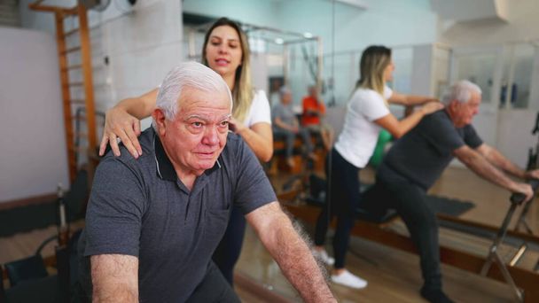 Senior Man Ćwiczenia w treningu z przewodnikiem, Pilates Studio Sesja z trenerką, osoba starsza korzystająca z maszyny do rozciągania, dbanie o zdrowie kręgosłupa - Zdjęcie, obraz
