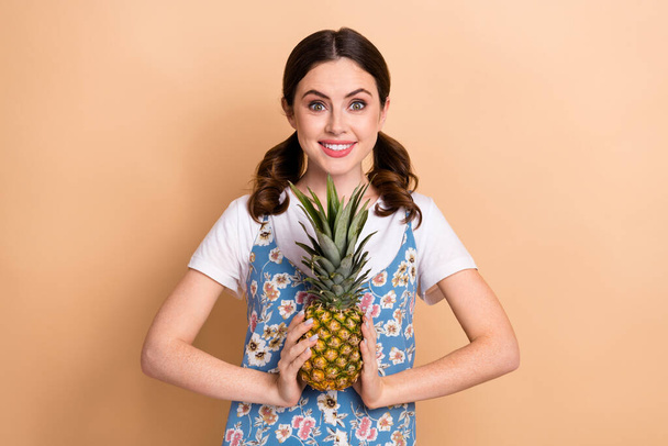 Photo of young girl funny curls ponytails wear dress presenting her favorite fruit pineapple sweet flavor isolated on beige background. - Foto, Imagen