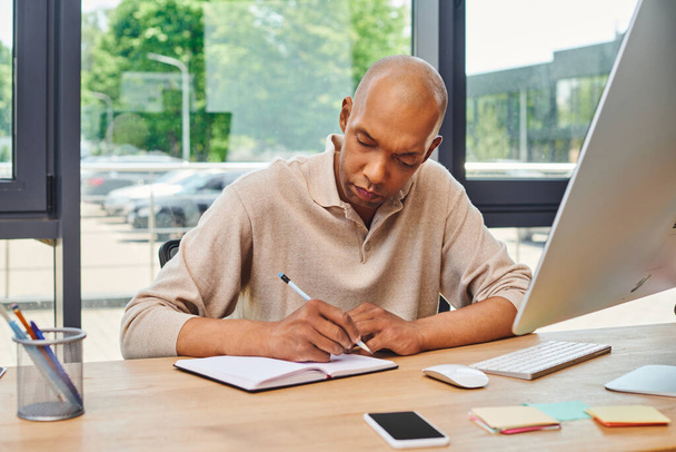 inclusion, african american man with myasthenia gravis at work, bold and dark skinned office worker taking notes, corporate culture, monitor and smartphone, computer mouse and keyboard on desk - Photo, Image