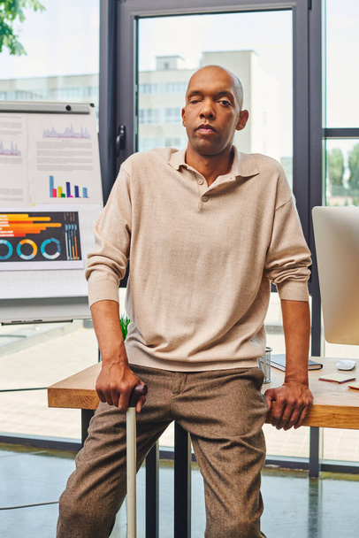 inclusión, síndrome de miastenia grave, negrita hombre de negocios afroamericano de pie con bastón cerca del monitor de la computadora en el escritorio de trabajo, trabajador de oficina de piel oscura en traje casual - Foto, Imagen