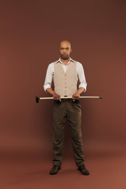 befogadás, merész afro-amerikai férfi myasthenia gravis szindróma gazdaság sétapálca, nézi a kamera, merész sötét bőrű férfi krónikus betegség álló barna háttér, teljes hosszúságú  - Fotó, kép