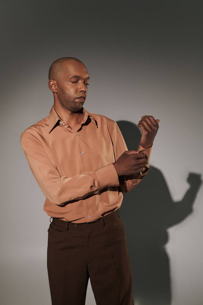 real people, bold african american man with myasthenia gravis standing on grey background, dark skinned person adjusting sleeve in shirt, smart casual, diversity and inclusion, physical impairment  - Foto, Bild