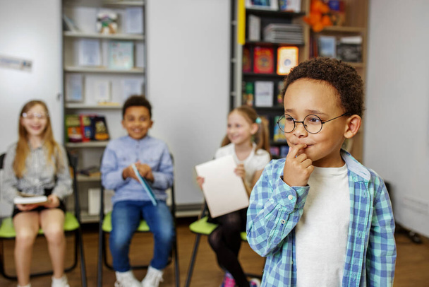 Un écolier afro-américain debout au milieu de la classe et répondant à une question devant ses camarades de classe et son professeur. - Photo, image