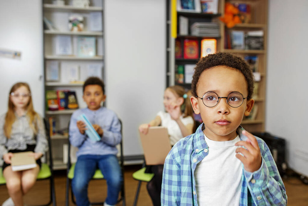 教室の真ん中に立って、クラスメートや先生の前で質問に答えるアフリカ系アメリカ人の少年. - 写真・画像