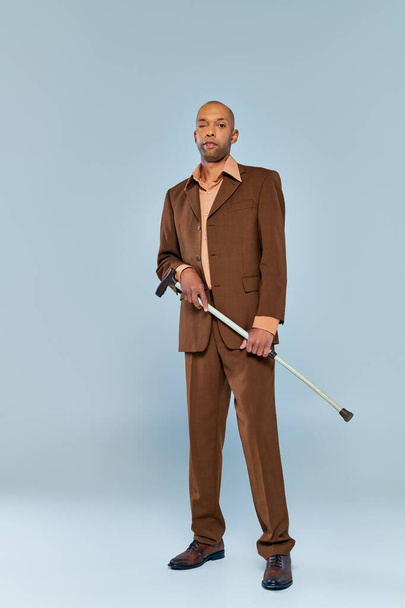 Синдром птоза, полная длина смелого африканского мужчины с миастенией на сером фоне, темнокожий человек в костюме, держащий трость, разнообразие и инклюзивность  - Фото, изображение
