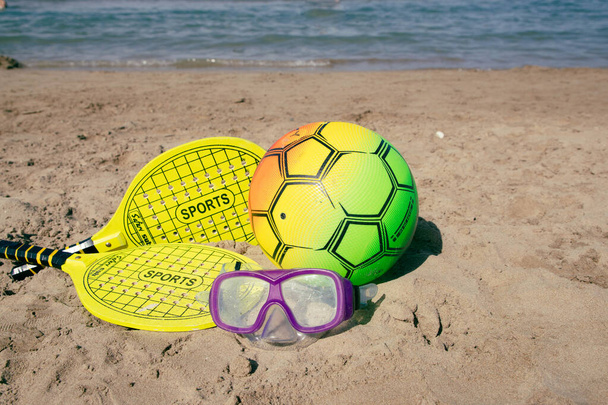Strandtennis racket en bal van gele kleur, zwemmasker, en beachvolleybal op het strand.Kopieerruimte.Zomer sport achtergrond. - Foto, afbeelding
