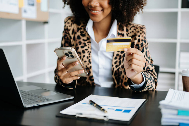 African Woman using smartphone for mobile payments online shopping,omni channel,sitting on table,virtual icons graphics interface screen  - Foto, afbeelding