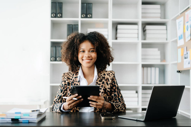 Junge Afrikanerin mit Laptop und Tablet an ihrem Arbeitsplatz. Konzentriert bei der Arbeit - Foto, Bild