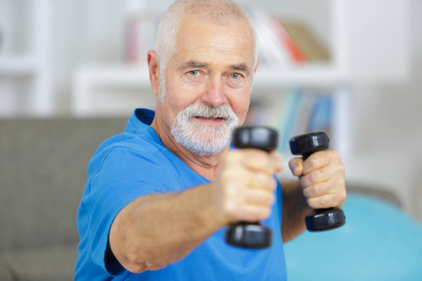 elderly man exercising with dummbells at home - Фото, зображення