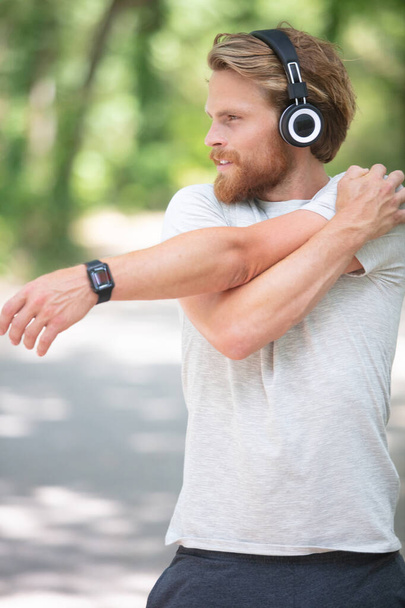 man wearing headphones is stretching in the park - Φωτογραφία, εικόνα
