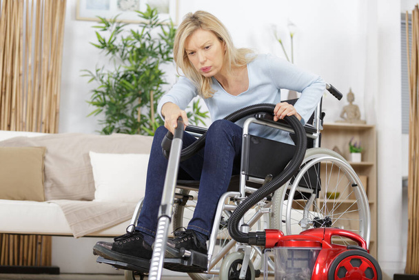 senior woman in wheelchair vacuuming a carpet - Photo, Image
