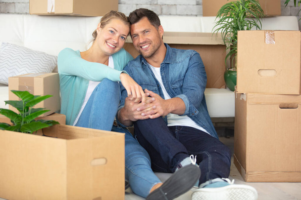 couple sitting on floor in new apartment around cardboard boxes - Фото, изображение
