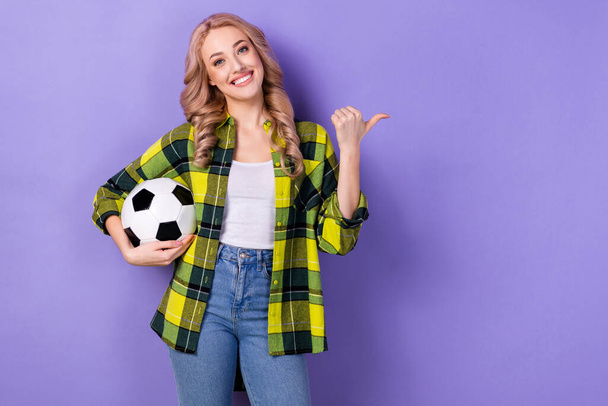 Photo of cute charming woman dressed checkered jacket holding ball pointing thumb empty space isolated purple color background. - Φωτογραφία, εικόνα