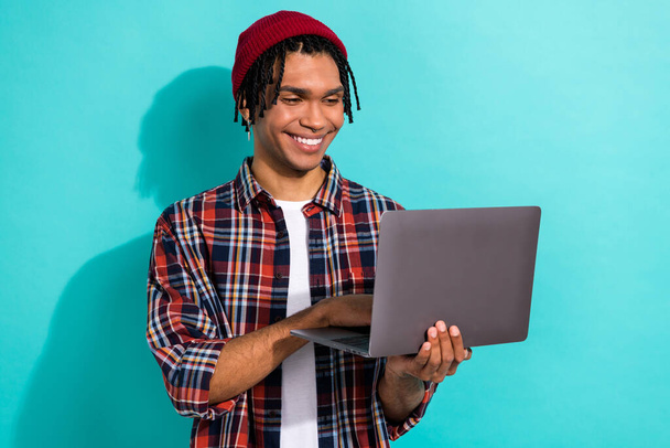Photo of toothy beaming cheerful guy with dreadlocks wear plaid shirt chatting hold modern laptop isolated on turquoise color background. - Fotoğraf, Görsel