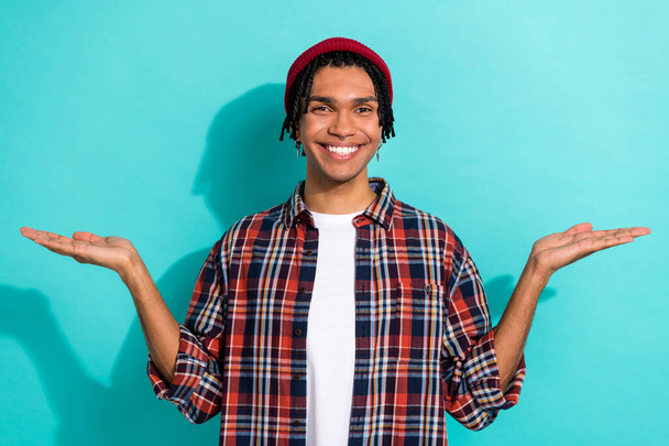 Foto portrét atraktivní mladý muž show palmy váhy objekty promo nosit módní kostkované oblečení izolované na akvamarínové barvy pozadí. - Fotografie, Obrázek