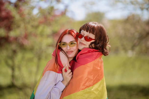 Happy lgbt couple in the middle of the park in a sunny day take the lgbt flag and walking through the grass together. lgbt - Foto, imagen