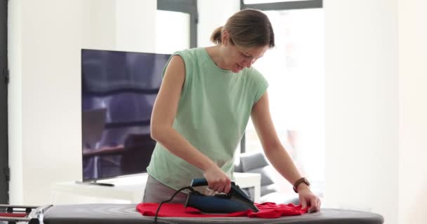Ženské tričko na žehlícím prkně. Žena ruka drží elektrické železo a domácí práce - Záběry, video