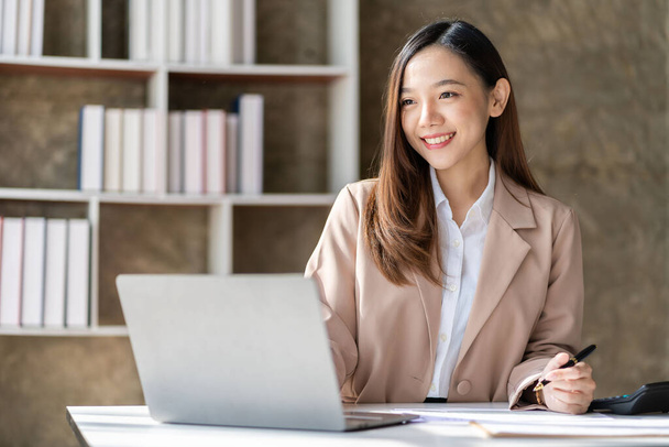 Beautiful asian businesswoman working with laptop and financial documents on desk, company employee holding accounting documents Checking financial data or market reports working in the office. - Photo, Image