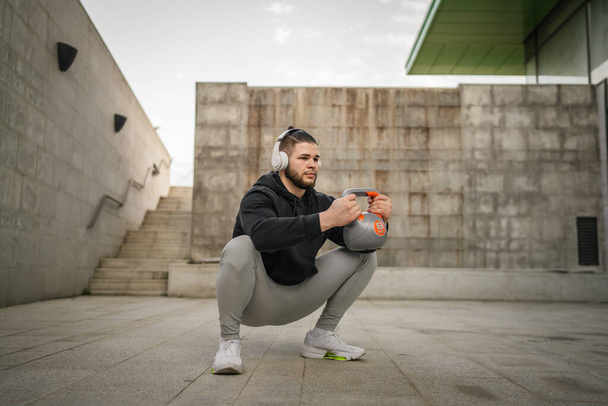Один человек молодой кавказский спортсмен стоит на открытом воздухе в дневной тренировке с русским колокольчиком Гиря гиревого веса упражнения реального человека копировать пространство - Фото, изображение