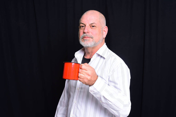 felnőtt férfi kávét iszik egy piros bögréből, kezében egy pohár folyadékkal - Fotó, kép