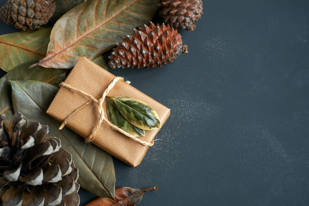 Paquetes de regalo de Navidad envueltos en papel artesanal y conos de pino con hojas secas - Foto, Imagen