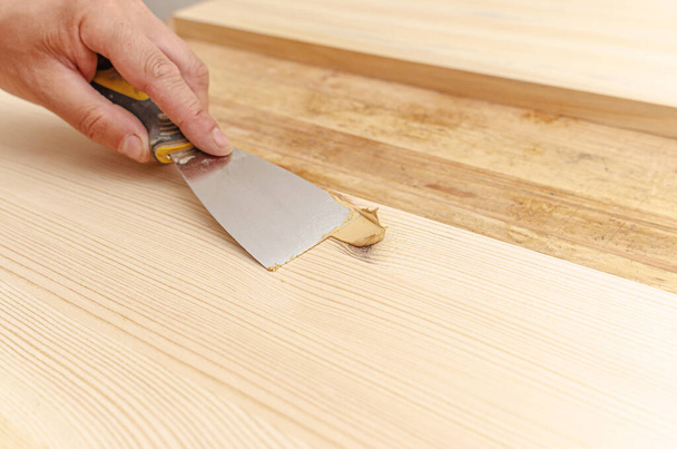 Covering knots on wooden board with putty. Spatula, putty, wooden board. Carpenter's hands. - Фото, изображение