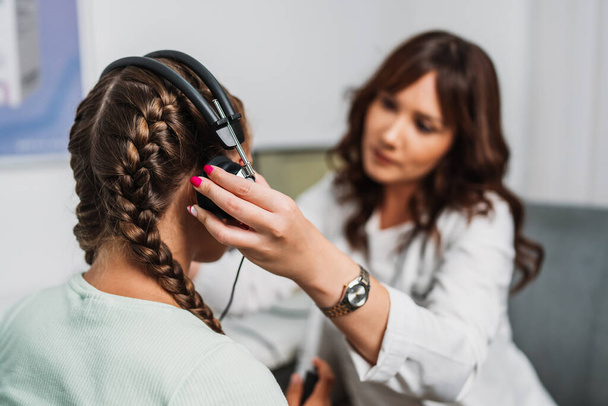 Audiologist doing impedance audiometry or diagnosis of hearing impairment. An beautiful teenage girl getting an auditory test at a hearing clinic. Healthcare and medicine concept. - Zdjęcie, obraz