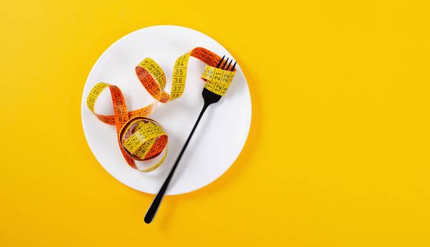 Diät, Abnehmkonzept, leere Platte mit Maßband und Gabel über gelbem Hintergrund - Foto, Bild