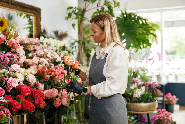 Donna fiorista fiorista proprietario del negozio di fiori tenere rose su sfondo floreale. Foto di alta qualità - Foto, immagini