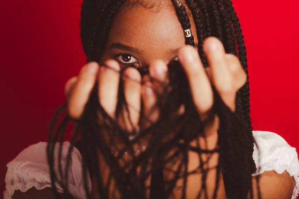 Retrato de cerca de una mujer negra con sus trenzas en la cara. Aislado sobre fondo rojo - Foto, Imagen