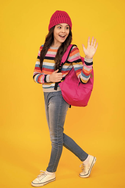School children in winter hat and sweater with school bag on isolated yellow studio background. Children learning and education. Happy teenager, positive and smiling emotions of teen schoolgirl - Photo, image
