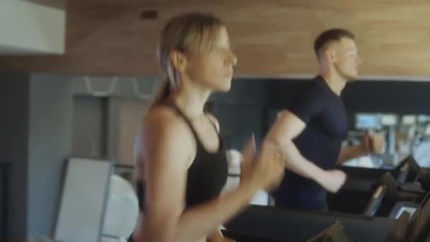 Waist up shot of sporty blonde woman running on treadmill while exercising in gym - Footage, Video