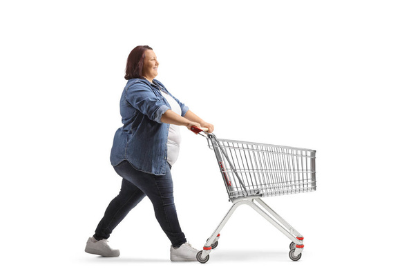 Täyspitkä profiili laukaus ylipainoinen naisentyöntää tyhjä ostoskori eristetty valkoisella pohjalla - Valokuva, kuva