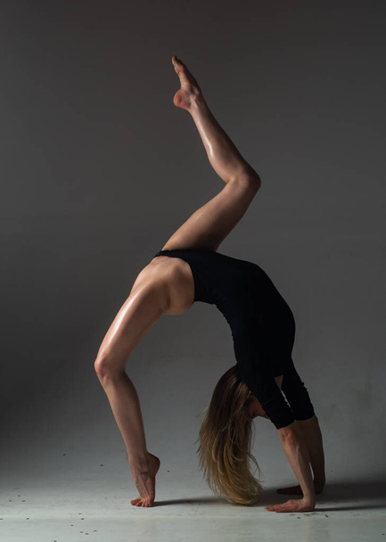 Sexy girl does gymnastic exercises for stretching. Beautiful sexy flexible woman demonstrates sexy flexible body. Flexibility stretching on black background. Strong flexible sexy female body - 写真・画像