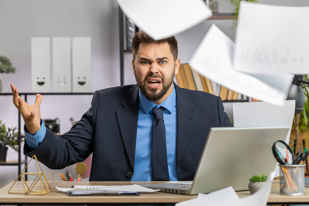 Stressed Caucasian businessman working looking at unpaid bank debt bills, doing paperwork, planning budget, calculate finances mortgage payments at office. Displeased freelancer man throws paper bills - Valokuva, kuva