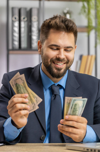 Rich businessman working on laptop counting money cash, calculate earnings income profit at home office workplace. Professional manager freelancer man. Business people. Employment occupation. Vertical - Foto, Imagen