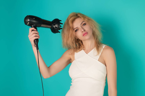 Young blonde woman with hair dryer on studio background. Hairs style and beauty concept. Beautiful girl with hairdryer drying hair. Beauty girl dries hair with hair dryer. Blow dryer - Фото, зображення