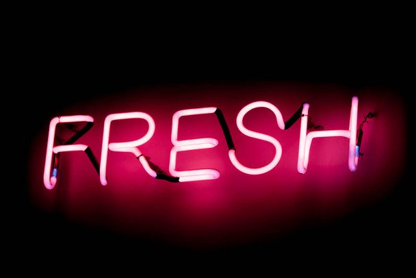 Una luz de neón rosa en forma de la palabra "Fresh" brillando sobre un fondo negro. - Foto, imagen