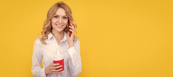 mujer rubia feliz con taza de café hablando por teléfono sobre fondo amarillo. Retrato de cara aislada mujer, pancarta con espacio de copia simulada - Foto, imagen