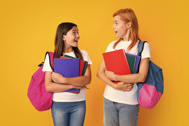 School, learning and education concept. Mother and daughter schoolgirls with school backpack and books ready to learn. Back to school. Mom and child on isolated yellow studio background - Photo, Image