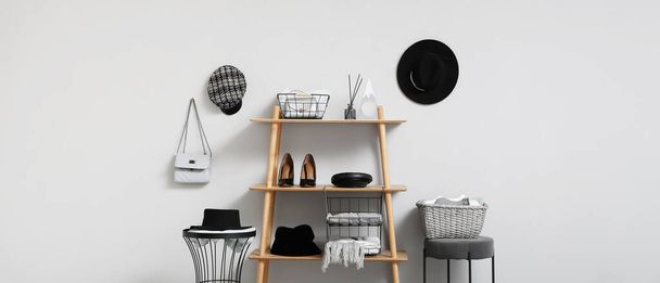 Wooden shelving unit with female clothes and accessories near light wall - Foto, afbeelding