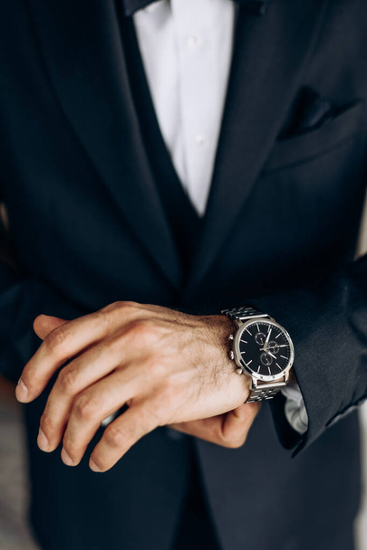 Der Mann trägt einen klassischen Anzug und eine teure Armbanduhr. Nahaufnahme einer mechanischen Uhr auf der Hand eines Mannes. Das Konzept von Pünktlichkeit und Vertrauen. Ein Mann legt seine Armbanduhr an - Foto, Bild