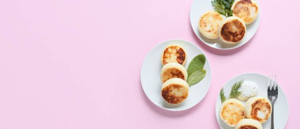 Platen met lekkere cottage kaas pannenkoeken en kruiden op roze achtergrond met ruimte voor tekst - Foto, afbeelding