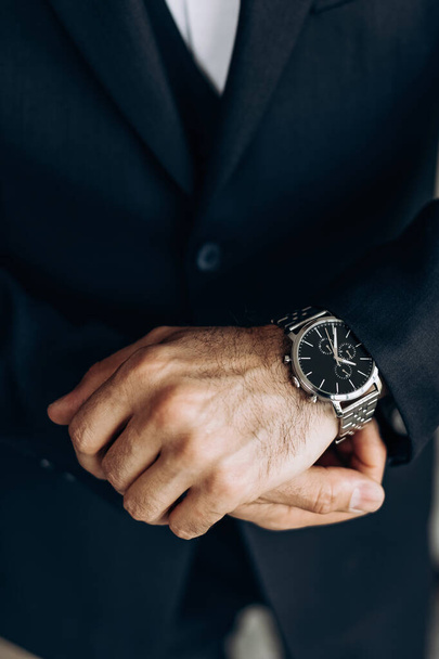 De man is gekleed in een klassiek pak en een duur horloge. Close-up van een mechanisch horloge op de hand van een man. Het concept van stiptheid. Accessoires voor heren in de vorm van een polshorloge - Foto, afbeelding