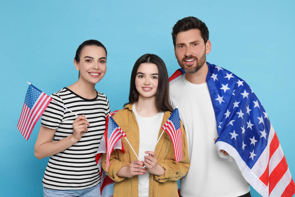 4 lipca - Dzień Niepodległości USA. Szczęśliwa rodzina z amerykańskimi flagami na jasnoniebieskim tle - Zdjęcie, obraz
