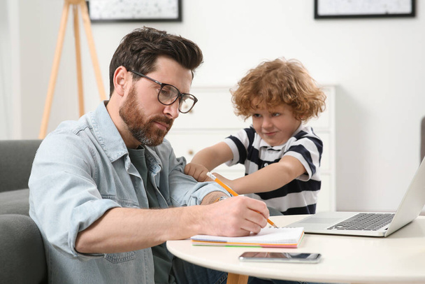 Little boy bothering his father at home. Man working remotely at desk - Foto, Imagem