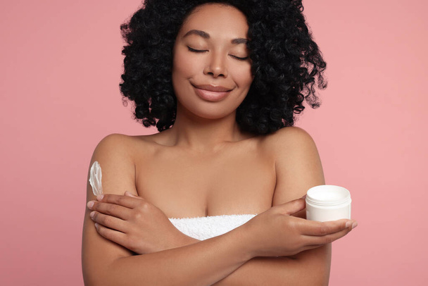 Young woman applying body cream onto shoulder on pink background - Fotó, kép