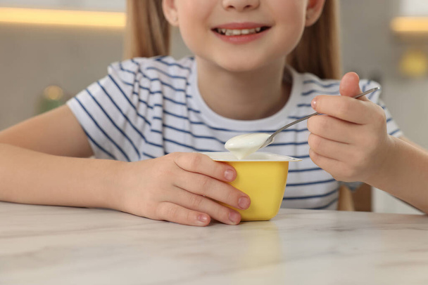 Cute little girl with tasty yogurt at white marble table, closeup - Foto, Bild