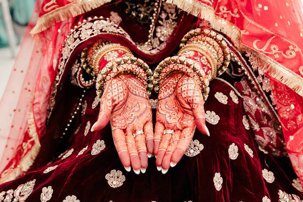 Las manos de la novia india están adornadas con patrones rojos rizados y joyas hechas de pulseras y anillos. Hermosos dibujos en el estilo indio de henna en las palmas de la novia - Foto, imagen